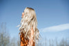 A blonde woman standing in front of a blue sky wearing QALI 100% remy clip in hair extensions